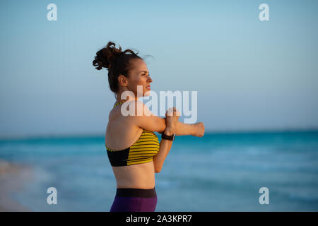 fitness sports woman in sport clothes on the ocean coast at sunset stretching. Stock Photo