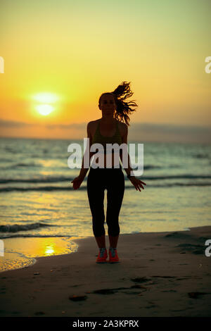 Silhouette of fitness sports woman in fitness clothes on the seacoast in the evening training. Stock Photo