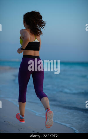 Seen from behind healthy sports woman in sport clothes on the beach in the evening jogging. Stock Photo