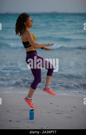 Full length portrait of young woman in sport style clothes on the seacoast in the evening workout. Stock Photo