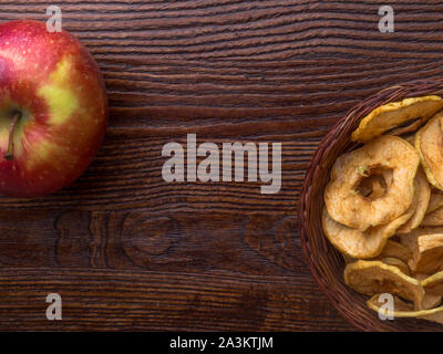 Healthy snack. Homemade dehydrated apple chips on rustic wooden background with fresh red apple Stock Photo