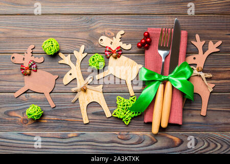 Top view of new year utensils on napkin with holiday decorations and reindeer on wooden background. Close up of christmas dinner concept .