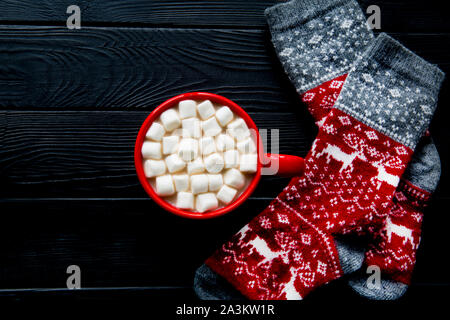 Winter hot beverage with marshmallow and red christmas ornament socks with deer on wooden black rustic table background. Copy space, space for text. Stock Photo