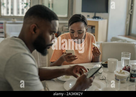 Distracted young African American couple using their cellphones over breakfast Stock Photo