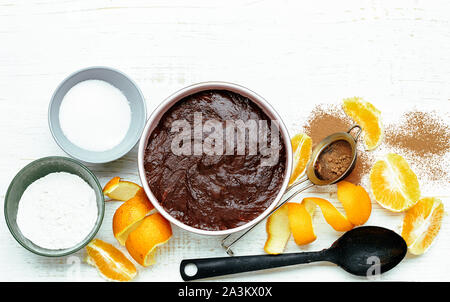 Baking ingredients of chocolate egg-free cake with orange juice and peel and kitchen utensil on white wooden table, flat lay, overhead top view, close Stock Photo