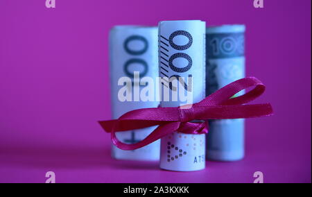 Banknotes of 200 Polish zloty rolled in roll and tied with red ribbon, behind two rolls of 100 zloty, concept of finacial  gift, purple background Stock Photo