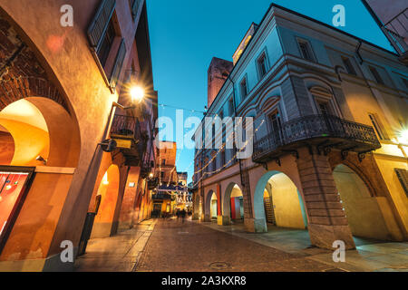 Cobblestone pedestrian street illuminated in evening in Old Town of Alba, Piedmont, Northern Italy (low angle view). Stock Photo