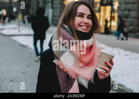 Happy young woman in warm clothing walking on city street during winter Stock Photo