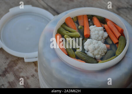 Homemade pickles, fermented vegetables. Pickled cucumber, cauliflower, carrot and bell pepper in pickle barrels on a rustic wooden table (Zimnica) Stock Photo