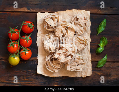 Whole wheat pasta tagliatelle, tomatoes and basil on a wooden background Stock Photo