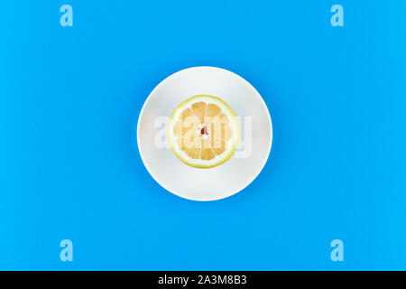 lemon on a blue background. lies on a white plate. half cut lemon. view from above. place to record. Lemon slices on a blue background. In summer Stock Photo