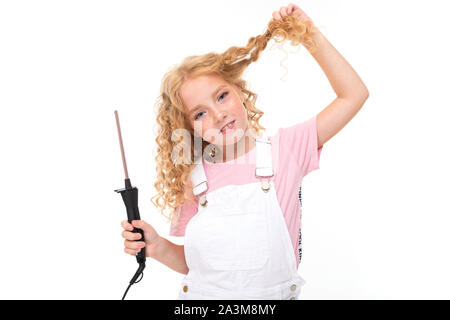 A little girl with red heap hair in a jersey, white jumpsuit, white sneakers spins her hair on a thin plow. Stock Photo