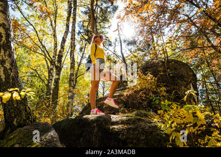 stylish woman in the autumn forest. A young beautiful girl stands on a stone against a background of yellow leaves and birches. Stock Photo
