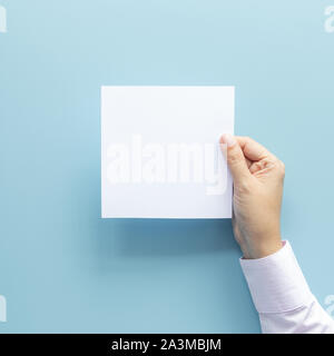 woman hand holding blank paper sheet isolated on blue background with copy space. Stock Photo