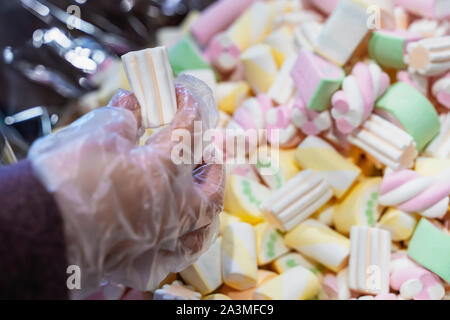 Multicolored marshmallow background. Texture. Top view. Hand in polyethylene glove holding marshmallow in confectionery store Stock Photo