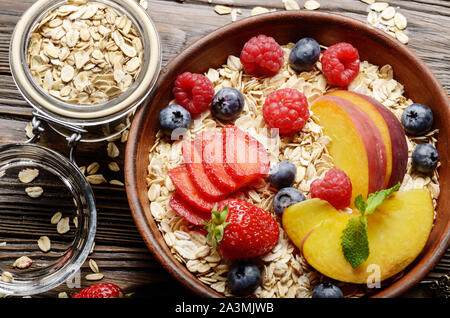 Flat lay of fruit healthy muesli with peaches strawberry almonds and blackberry in clay dish on wooden kitchen table Stock Photo