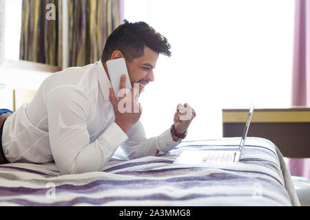 Young businessman celebrating success with raised arms, staying in hotel Stock Photo