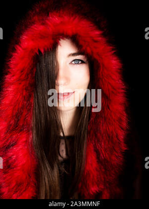 beautiful young Russian woman with blue eyes and brown hair wearing red faux fur coat with hood on her head Stock Photo