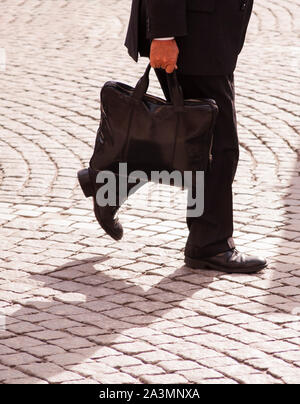 man in business suit walking down cobblestone square Stock Photo