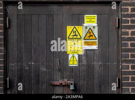 Workplace safety: caution Danger of Death triangular warning signs on town centre substation; Copper earth cable has been removed from this electricty substation, Southport, UK Stock Photo