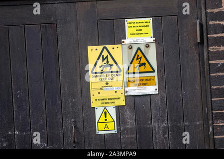 Workplace safety: caution Danger of Death triangular yellow warning signs on town centre substation; Copper earth cable has been removed from this electricity substation, Southport, UK Stock Photo