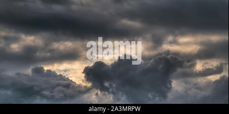 Panoramic shot of the autumn sky with huge heavy clouds of gray-blue color and the rays of the sun. Stock Photo