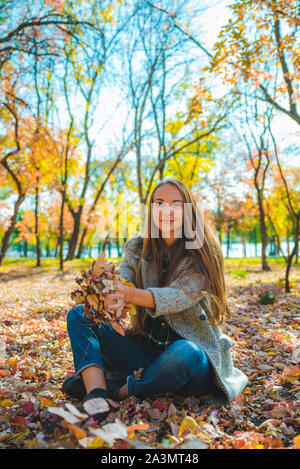 young pretty woman playing with yellow autumn leaves at city park Stock Photo