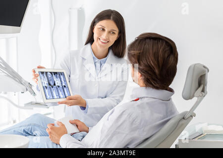 Beautiful dentist showing his patient x-ray results on digital tablet Stock Photo
