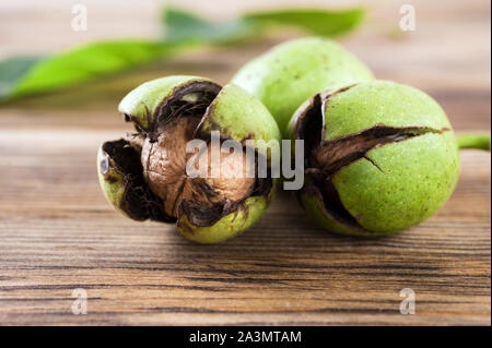 Three ripe raw walnuts with green shell on the wooden table Autumn nuts..Selective focus.Horizontal orientation. Stock Photo