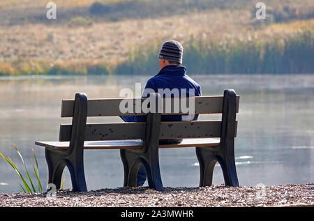 A man sits on a quiet bench along a misty river in early morning, reading a magazine, in central Oregon. Stock Photo