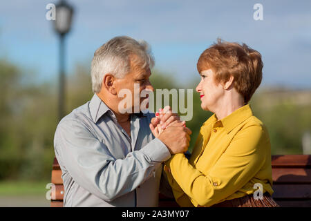 Mature lovers hug tightly bench in a city park. Stock Photo