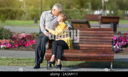 Mature lovers hug tightly on a bench in city park Stock Photo