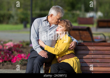 Mature lovers hug tightly on a bench in a city park. Stock Photo