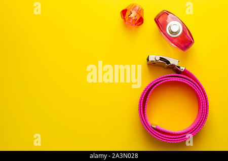 Pink belt and perfume bottle on yellow with copy space. Summer background concept. Stock Photo