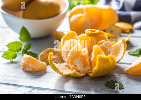 Tangerines with peel and mellisa herbs on table. Ripe fresh tropical fruit on wooden board Stock Photo