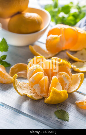 Tangerines with peel and mellisa herbs on table. Ripe fresh tropical fruit on wooden board Stock Photo