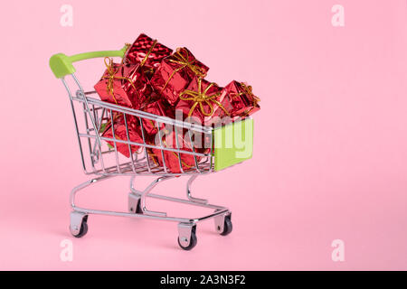 Shopping cart full of gifts of red color on a pink background, with a negative space Stock Photo