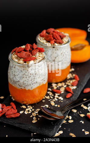 Chia seed yogurt pudding with goji berries, smashed fresh apricot and oats on black background. Healthy balanced food concept Stock Photo