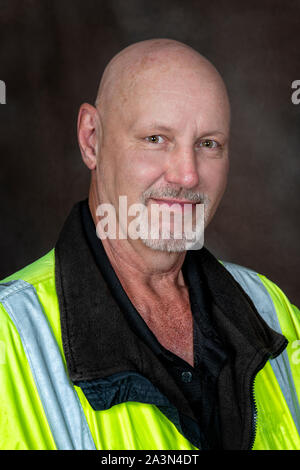 Vertical shot from the chest up of a friendly mature male worker in reflective clothing.  Brown background. Stock Photo