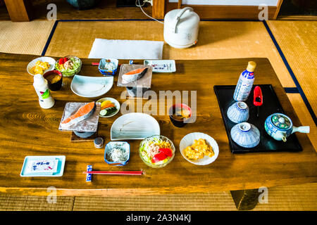 Ichi-ju-san-sai, a traditional Japanese breakfast of miso soup and several small side dishes, is laid out on a low wooden table at Ryokan Izu Makiba, Nishiizu-Cho, Shizuoka Prefecture, Japan. Rice, grilled salmon, pickled vegetables and tea are arranged on the tatami floor. Stock Photo