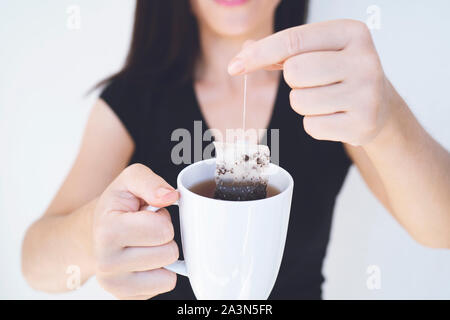 Hands of a young woman holding a cup. Herbal tea bag cup in hand on white background isolation Stock Photo