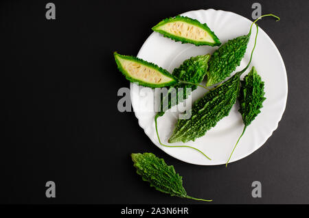 Bitter cucumber on white plate on black background. Cooking concept. Copy space, top view.