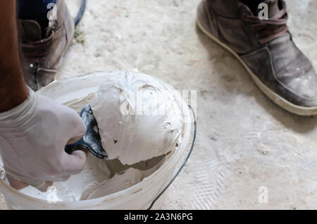 A worker in gloves using a putty knife to take a putty solution for construction. Stock Photo