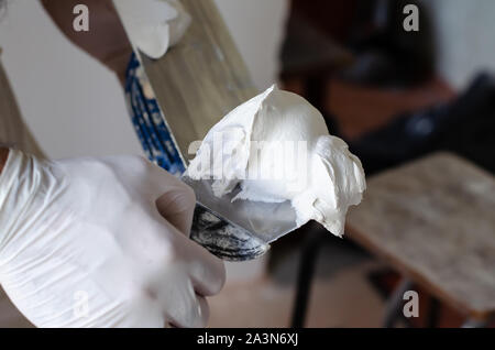 A worker in gloves using a putty knife to take a putty solution for construction. Stock Photo