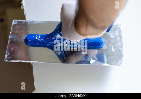 Wall putty concept. A worker in gloves working with spatula or putty knife. Stock Photo