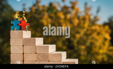 Teamwork concept. The concept of victory. Two puzzles stand at the top of the stairs made of wooden blocks with blurred autumn sunny background. Stock Photo