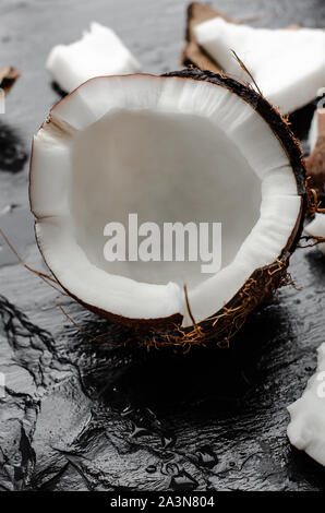 Coconut half on black slate stone background. Nutrition concept. Vertical Stock Photo