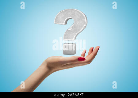 Stone question mark in air above woman's open palm on light-blue gradient background. Stock Photo