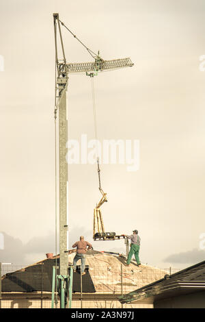 vertical image of construction workers on the roof, two men working with the crane Stock Photo
