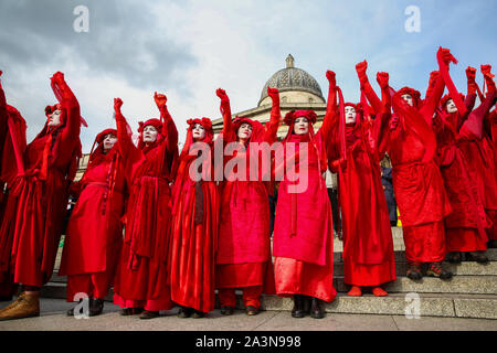Members of Red Brigade from Extinction Rebellion movement in their costumes protesting on the steps of Trafalgar Square during the third day of their two weeks action in Westminster. The climate change activists are calling for the UK Government to take urgent action on climate change. Stock Photo